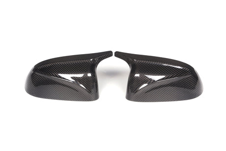 Two carbon fiber side mirror covers are positioned side by side, slightly angled inward, on a plain white background, showcasing their glossy, textured surfaces.