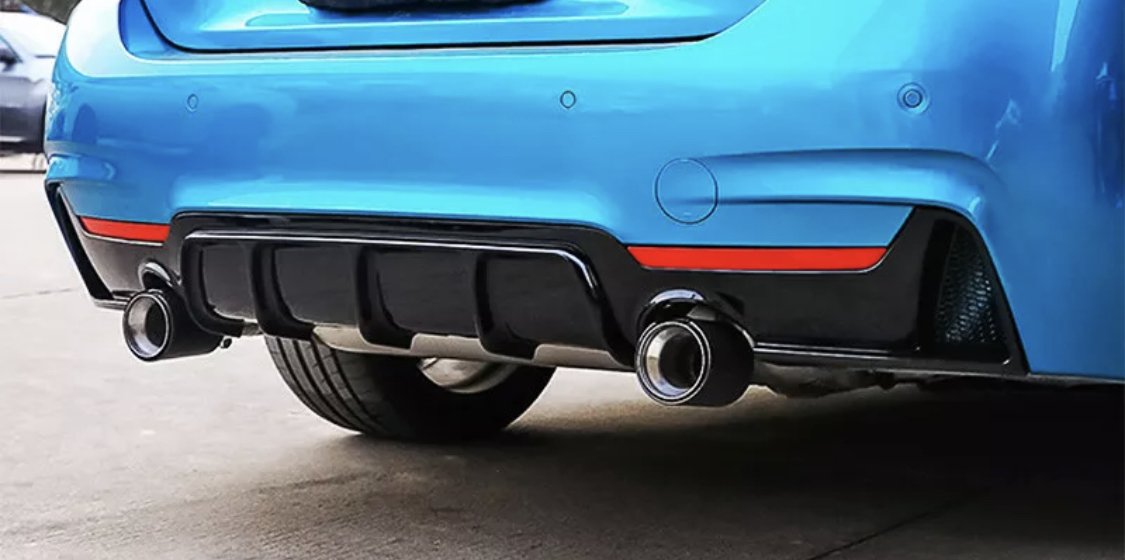 A blue car's rear features dual exhaust pipes and a black diffuser with red accents, parked on concrete.