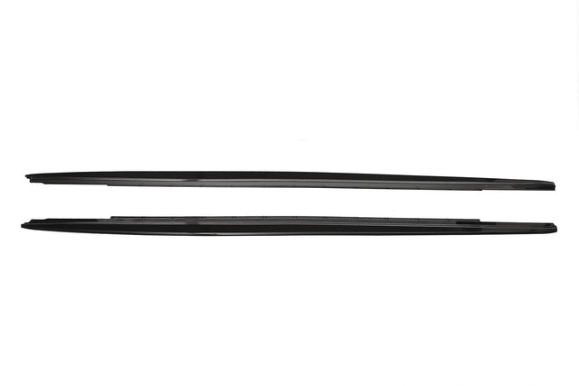 Two sleek, black car side skirts, aligned horizontally, lie against a plain white background, showing their aerodynamic design and smooth edges.