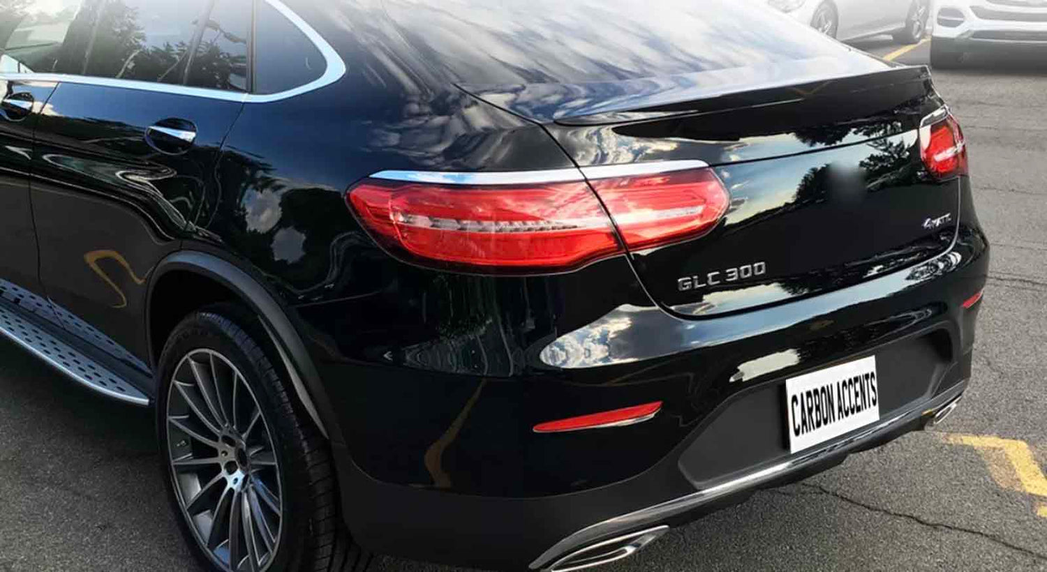 A black car is parked in a lot, reflecting clouds. The license plate reads "CARBON ACCENTS." The model text "GLC 300" and "4MATIC" appears on the rear.