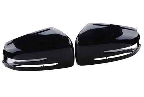 Glossy black car side mirror covers lie face up, displaying their sleek, aerodynamic shape. Positioned parallel to each other, they rest on a white, featureless background.
