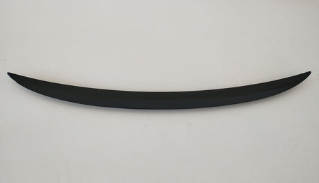 A curved, sleek, black object rests horizontally on a plain, light-colored background, resembling a minimalist sculpture or car spoiler.