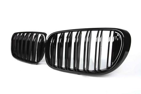 Two glossy black car grilles with vertical slats are displayed against a plain white background. The design suggests modern automotive styling.