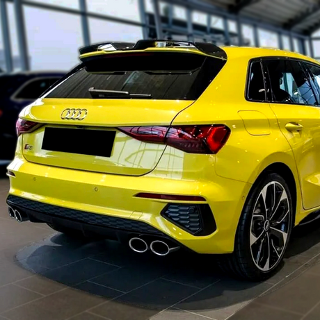 A bright yellow car is parked indoors, featuring twin exhausts and a rear spoiler. The Audi logo and "S3" badge are visible on the back, within a showroom environment.