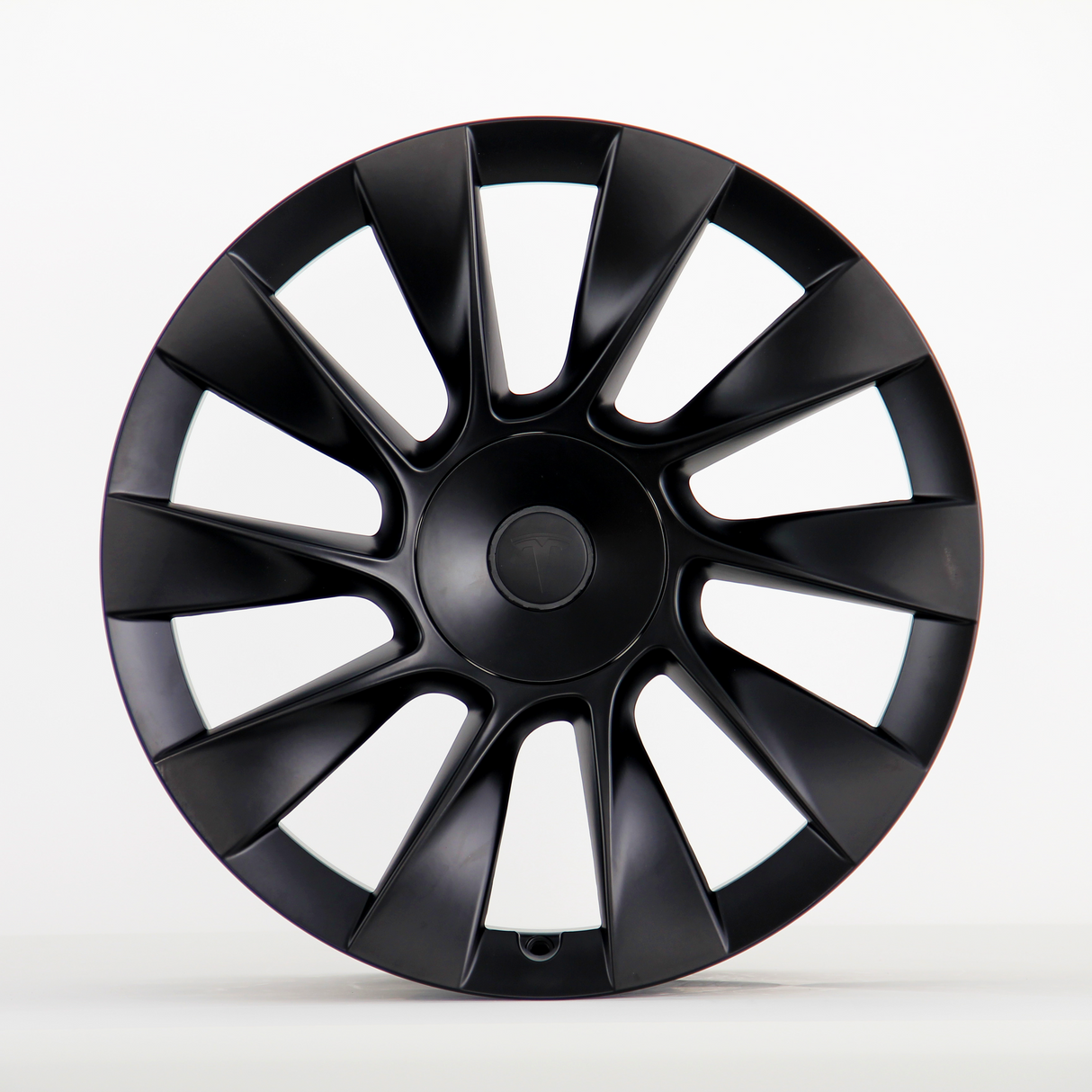 A black, multi-spoke car wheel cover with a subtle central logo sits upright against a plain white background, showcasing its sleek, aerodynamic design.