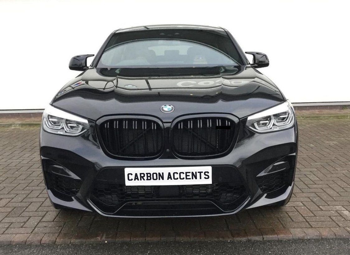 A black BMW car is parked on a brick surface, facing forward. The front grille and headlights are prominent. Text on the license plate reads, "CARBON ACCENTS."