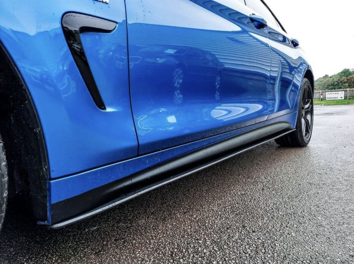 A blue car, parked on a wet asphalt surface, shows its glossy side panel and black wheel, with reflections of nearby structures visible. A sign in the background reads "SEVEN PARKING."