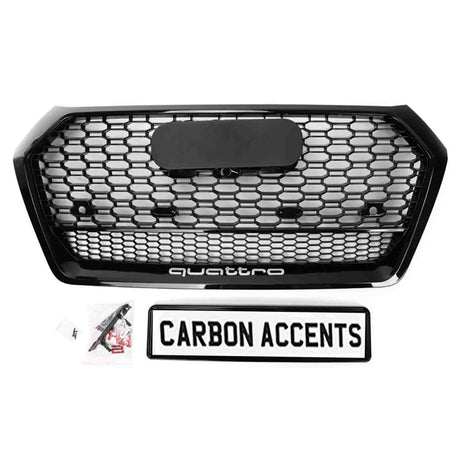 A black honeycomb car grille labeled "quattro" sits on a white background. Below it, a rectangular sign reads "CARBON ACCENTS," accompanied by several small plastic bags with parts.