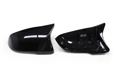 Two glossy black side mirror covers are placed side by side on a plain white background, with the right one showing an interior label.