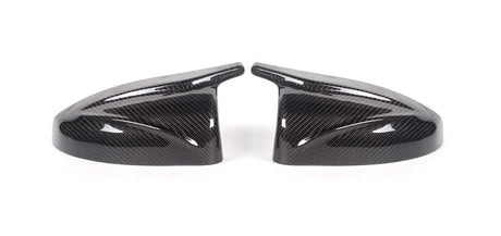 Two carbon fiber side mirror covers rest on a white surface, showcasing a glossy finish and intricate weave pattern, appearing symmetrically aligned.