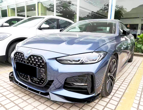 A sleek blue car is parked on a tiled surface outside a dealership, alongside a white vehicle. Large windows and plants are visible in the background, reflecting a modern setting.