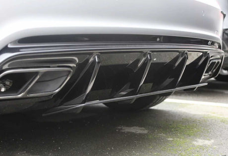 The image features a car's rear diffuser with fin-like protrusions, enhancing aerodynamics. It is parked on an asphalt surface, visible in the background.