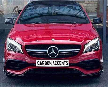 A red Mercedes-Benz car is parked inside a building, facing forward. The license plate reads "CARBON ACCENTS." The car's headlights are on, and reflective windows surround the scene.