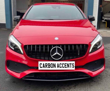 A red car featuring a prominent front grille and sleek headlights is parked outside a garage. The license plate reads "CARBON ACCENTS."
