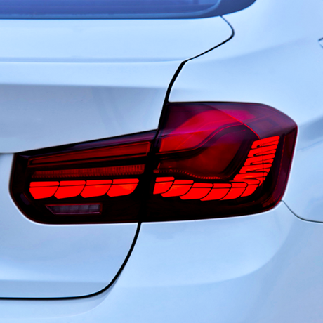 A car's right rear taillight is illuminated red, indicating its stop or parked status, attached to a sleek, white vehicle body with smooth contours and defined lines.