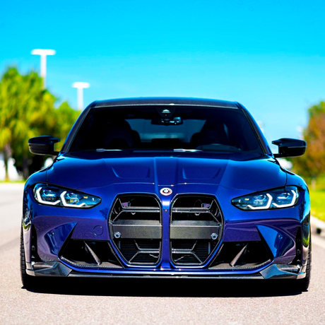 A blue sports car is parked on an empty road, showcasing its aggressive front grille and headlights. The sunny day highlights the car's sleek design, with trees in the background.