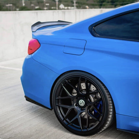 A blue sports car is stationary on a rooftop parking lot, highlighting its rear wheel with glossy black rims and a sleek spoiler.