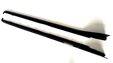 Two elongated black metal car side skirts lie parallel on a plain white surface, featuring multiple mounting holes along their length and slight contours for aerodynamic enhancement.