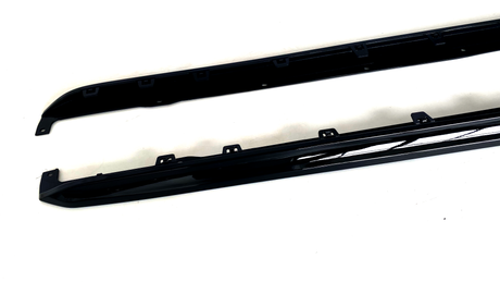 Two black car side skirts are resting on a white surface, featuring several mounting brackets along their length for attachment.
