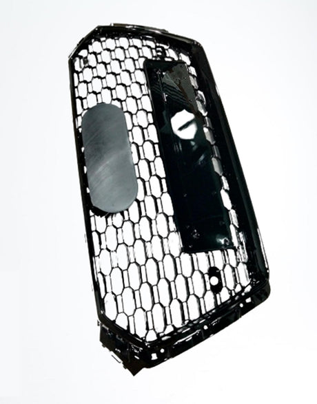 A hexagonal-patterned car grille with a glossy black finish is tilted vertically. It contains a central oval emblem holder, and is isolated against a plain white background.