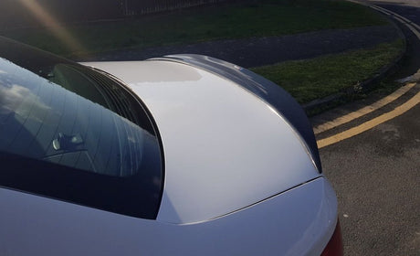 A silver car with a reflective rear window and smooth surface is parked on a street with yellow double lines, beside a grassy verge and paved sidewalk.