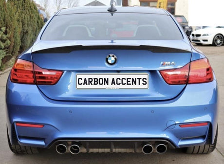 Car viewed from the rear, displaying a blue BMW M4 with dual exhausts; the license plate reads "CARBON ACCENTS." It is parked on a street lined with trees and other cars.