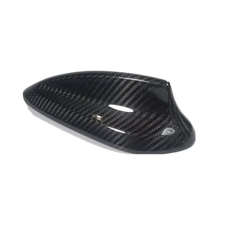 A carbon fiber car mirror cover, featuring a glossy, black textured surface, rests against a plain white background, highlighting its sleek design and curved aerodynamic shape.