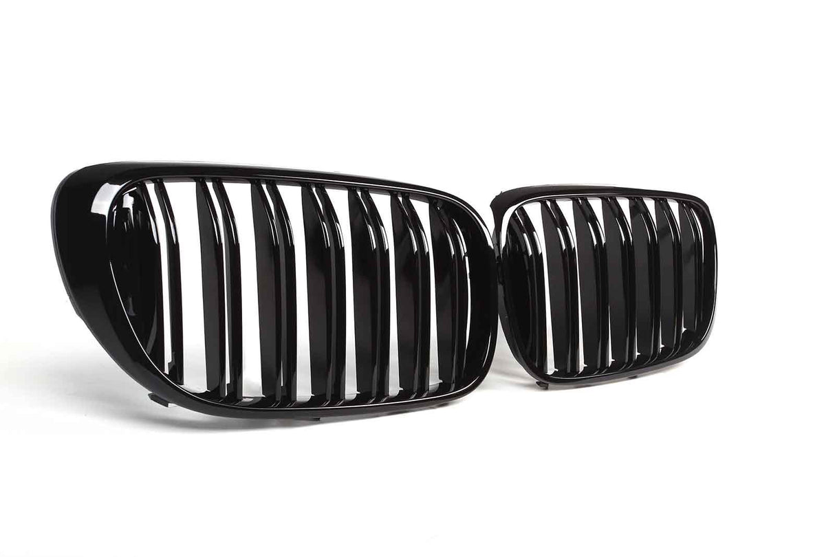 Two glossy black car grilles with vertical slats are positioned side by side, resting on a clean, white surface.