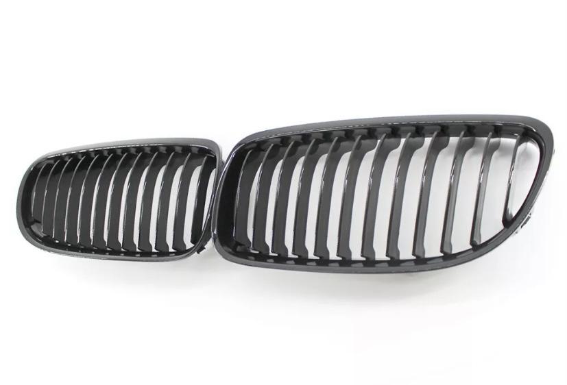Two black car grille inserts with vertical slats lie side by side on a white background, resembling classic automotive front grille designs.