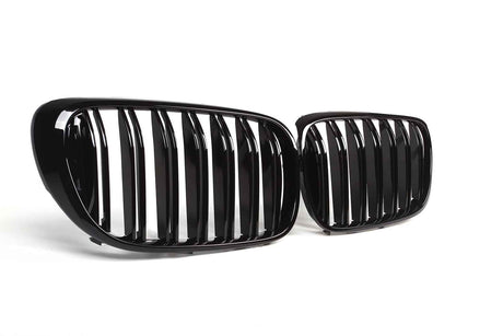 Two glossy black car grilles, featuring vertical slats, are positioned on a plain white background, angled slightly toward each other.