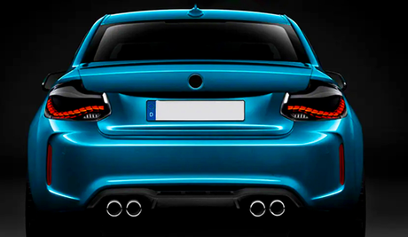 A sleek blue sports car is shown from the rear, featuring illuminated taillights and dual exhausts, set against a dark background. The license plate reads "D."
