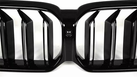 Black car grille with vertical slats is centered with a circular camera. It is positioned against a clean, white background, emphasizing its sleek, modern design.