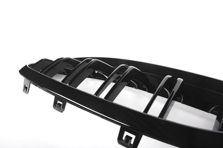 A glossy black car grille with vertical slats rests against a bright white background, featuring attachment clips at the bottom edge.