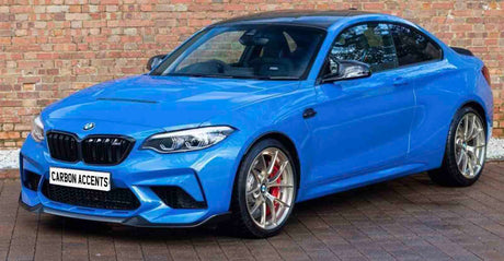 Bright blue sports car parked on brick pavement, with silver alloy wheels and tinted windows, positioned in front of a brick wall. License plate reads "CARBON ACCENTS."