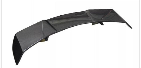 A curved carbon fiber car spoiler rests on a flat surface. The piece features aerodynamic design elements, such as a high-gloss finish and multiple support fins.