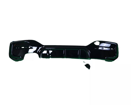 A black car bumper lies flat against a white background. The bumper has several cutouts for attachments, and a small disconnected component rests nearby.