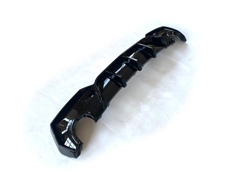 A glossy black car diffuser with several fins lies on a white surface, designed for aerodynamic enhancement.