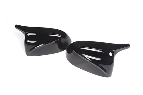 Two glossy black aerodynamic mirror covers lie on a white surface, their sleek, curved design reflecting light, indicating they are automotive accessories.