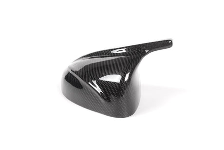 A glossy, black carbon fiber vehicle mirror cover is placed on a plain white background, showcasing its sleek, aerodynamic design and lightweight material.