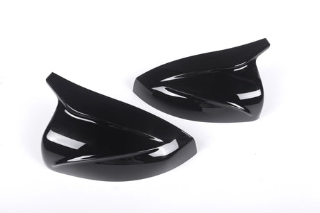 Two sleek, black, aerodynamic car mirror covers lay side by side on a plain white background, emphasizing their glossy finish and curved design.