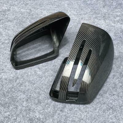 Carbon fiber car mirror covers rest on a gray carpet. One cover is upright, showing slot designs, while the other is on its side, revealing the inner structure.