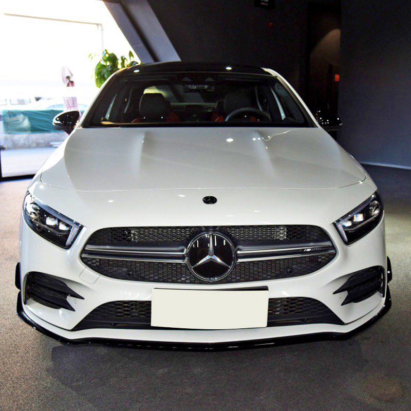 A white Mercedes-Benz car is parked indoors on a carpeted floor, with natural light coming from a left-side window, highlighting its front grille and logo.