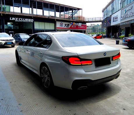A silver sedan, parked, in an urban setting with adjacent shops and cars. Prominent signage above the shops includes "LIKE CLUB" and other Chinese text.