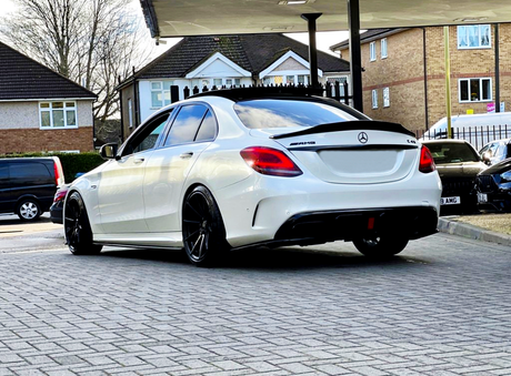 A white Mercedes-AMG C43 with black rims is parked under a canopy, surrounded by residential buildings.