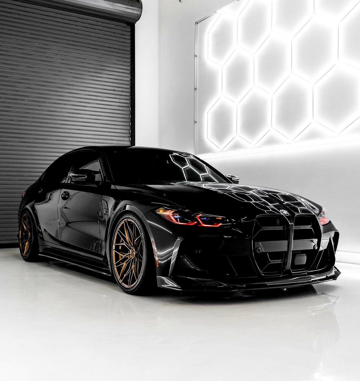 A sleek black car with bronze wheels is parked in a dimly lit, modern showroom with hexagonal wall lights, creating a reflective pattern on the car's surface.