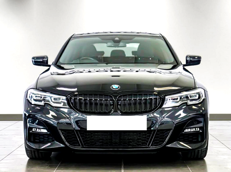 A black car with a sleek design and prominent front grille is parked indoors against a plain white backdrop, emphasizing its modern aesthetics.