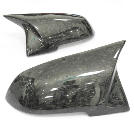 Two glossy, dark carbon fiber car mirror covers resting on a plain white background, highlighting their sleek design and textured surface reflecting light.