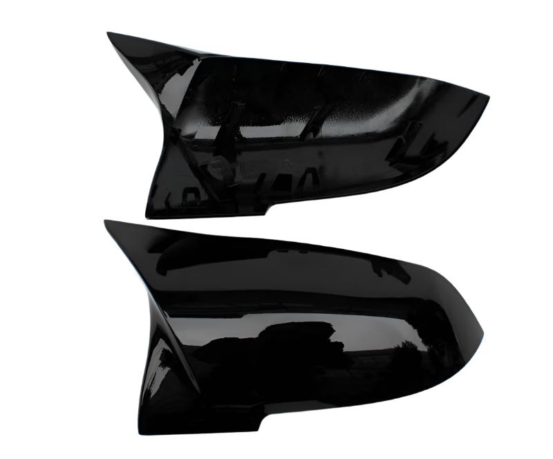 Two black, shiny car mirror covers are displayed against a white background. The top cover shows its inner side with attachment points, while the bottom displays a smooth exterior surface.
