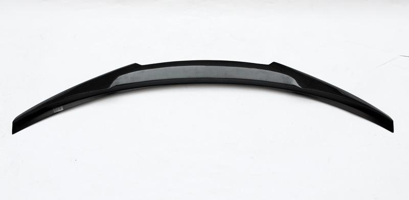 A curved black car spoiler, with a carbon fiber texture in the center, lies on a plain white background.