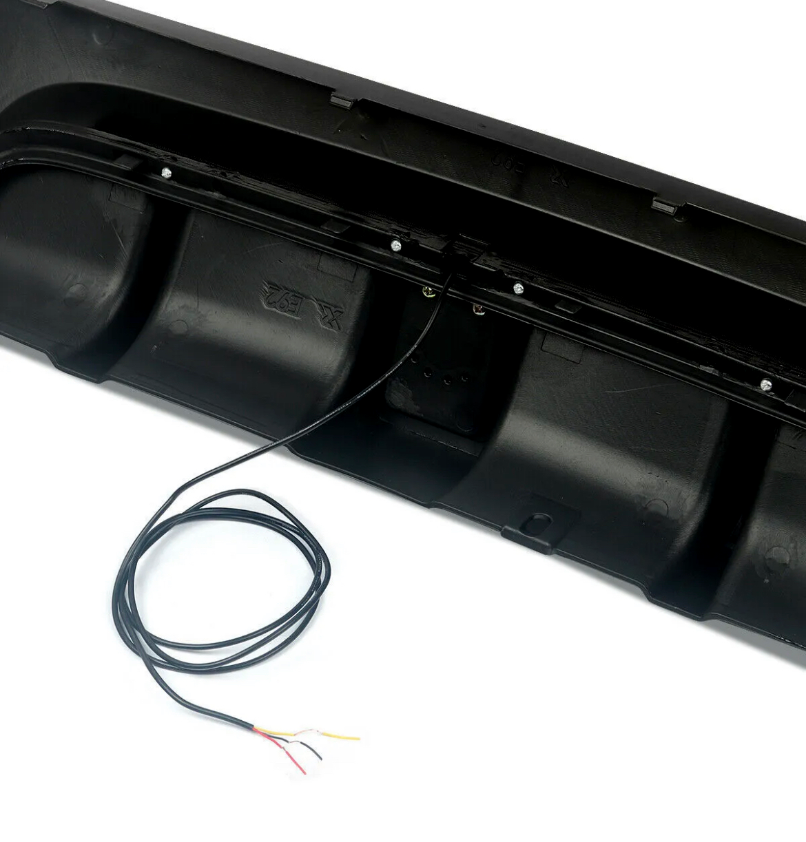Black bumper with visible wiring extending from it, placed on a smooth white surface, partially covered by a coiled black cable with exposed colored wires.